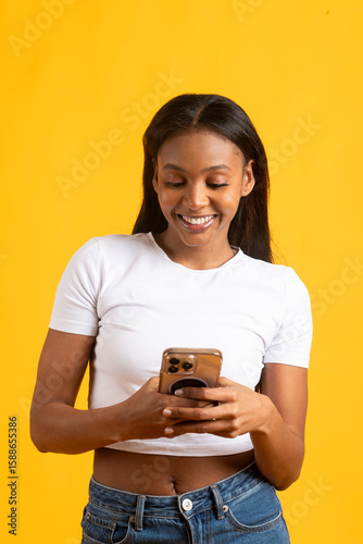 Smiling young woman using smartphone on yellow background