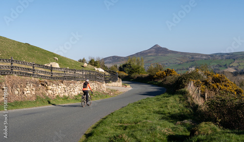 Weekend getaway. A female cyclist rides through the mountainous landscape of Wicklow, Ireland, with Sugar Loaf Mountain on the horizon.