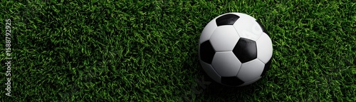 A classic black and white soccer ball rests on vibrant green artificial turf under bright lighting.