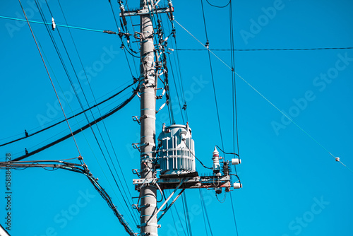 A utility pole with a transformer and many power lines against a clear blue sky.
