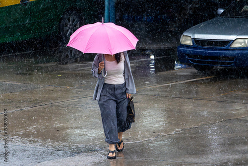 A woman walks in the rain on a wet street, carrying a pink umbrella.