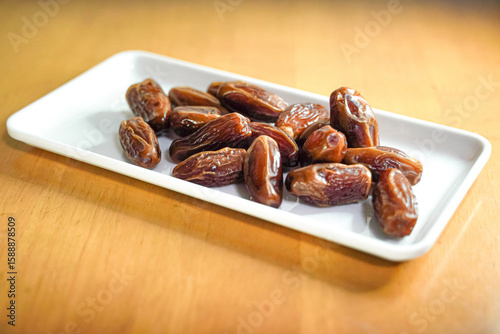 Close-up view of a white rectangular plate filled with dried dates, presented on a wooden surface.