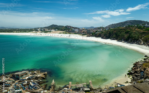 Fototapeta Naklejka Na Ścianę i Meble -  Part of Praia Grande, with green and blue waters, a small fishing village, beautiful blue sky and the city in the background. Located near the city of Cabo Frio, Rio de Janeiro, Br