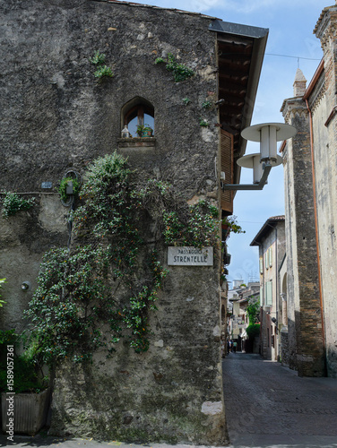Charming Corner In Sirmione Adorned With Greenery With Historic Buildings And Sign, Italy