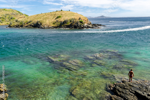 View of part of Praia do Forte, with lots of rocks and crystal clear waters all along the beach, mountains in the background and boats sailing. Cabo Frio, Rio de Janeir-Editar