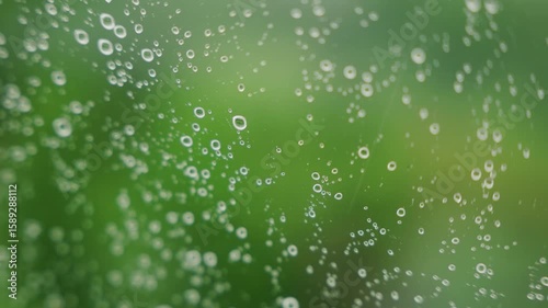 Close-up view of raindrops on glass, showcasing a blurred green background, creating a serene and refreshing atmosphere