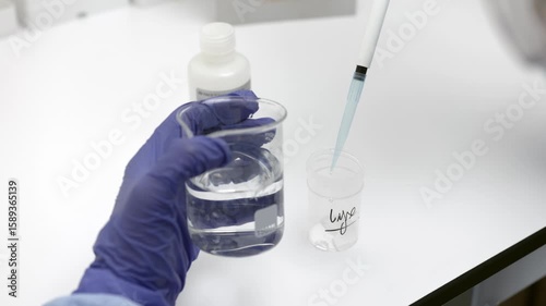 scientist using pipette to transfer liquid from glass beaker into plastic container during laboratory experiment in sterile environment with gloves and lab tools