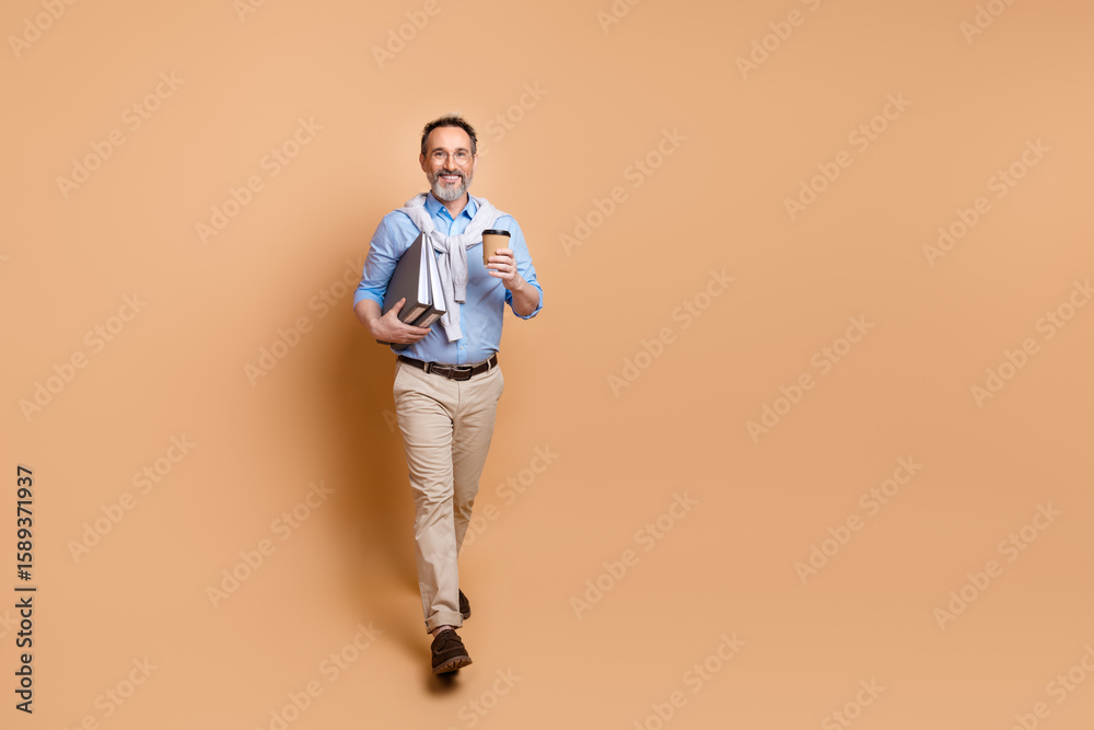Fototapeta premium Confident senior businessman with books and coffee enjoys elegant casual style against a beige background