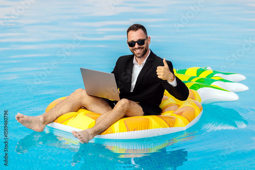 Businessman in a suit sitting on a pineapple-shaped inflatable, working on a laptop in a pool. Concept remote work, summer, contrast.