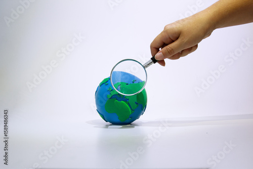 Hand Examining Earth Globe with Magnifying Glass. Human hand holding magnifying glass over earth model symbolizing environmental research and planet examination. Earth day concept. 