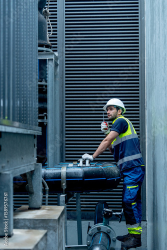 Vertical image of engineer or technician worker hold  walkie talkie and stand with looking and maintenance during work with steel pipe system of factory building.