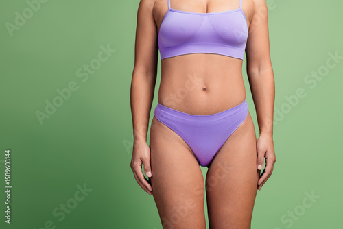 Slim African American woman posing naturally on a green background in stylish lilac lingerie emphasizing body positivity