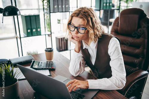 Billede på lærred Businesswoman in an office wearing formal attire works on a laptop displaying a