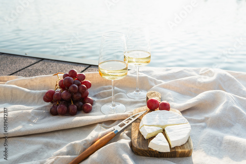Two glasses of white wine with cheese and grapes on a pier at sunset.