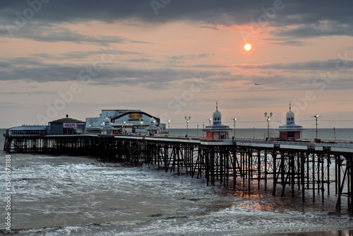 Blackpool North pier at sunset with a red dramatic sky reflected on the sea with an incoming tide