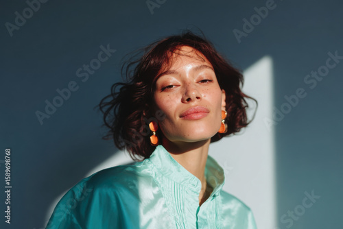 Fashion model posing in sunlight with turquoise shirt and orange earrings