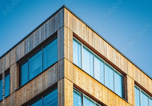 A closeup view of a modern office building facade with glass windows reflecting the clear blue sky, emphasizing contemporary architecture and urban design elements.