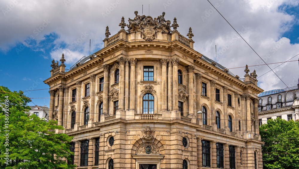 Fototapeta premium Baroque Architecture In Munich: Ornate Historic Building With Sculpted Facade, Arched Windows, Decorative Columns, And Stone Details Under Blue Sky With Clouds In Vibrant Urban Cityscape