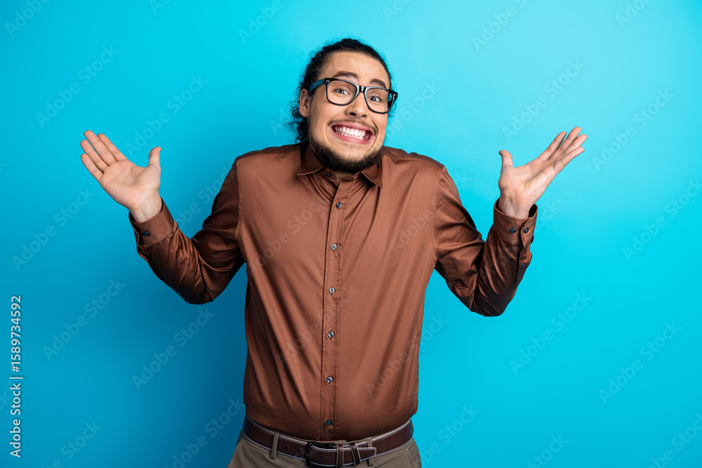 Naklejka premium Young stylish man in brown formalwear making a humorous shrug gesture against a vibrant teal background