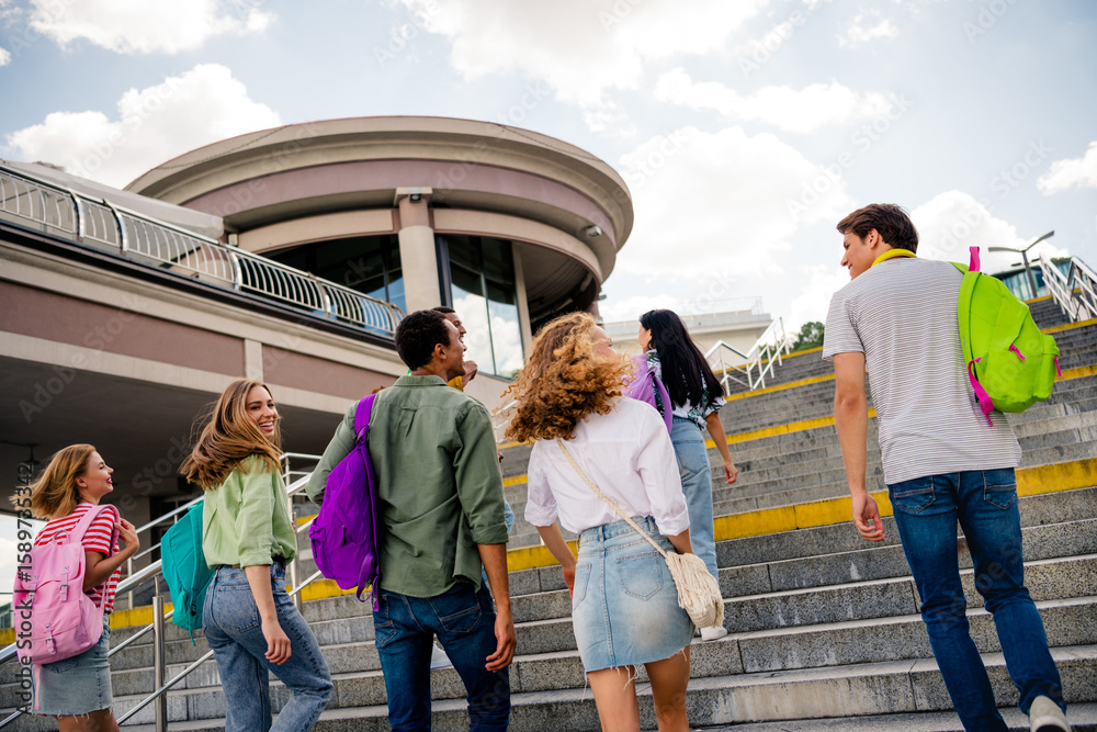 Obraz premium Group of cheerful students walking outdoor on a sunny day carrying backpacks at a modern urban campus