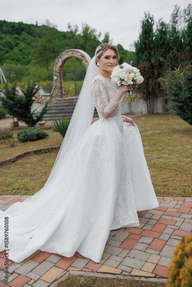 Fototapeta premium Elegant bride poses outdoors in stunning gown with bouquet during wedding preparations