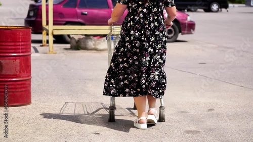 Woman Slowly Pushing Shopping Cart on Street on a Summer Day