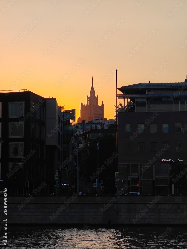 Fototapeta premium Beautiful sunset over city skyline with iconic tower rising above buildings near a river