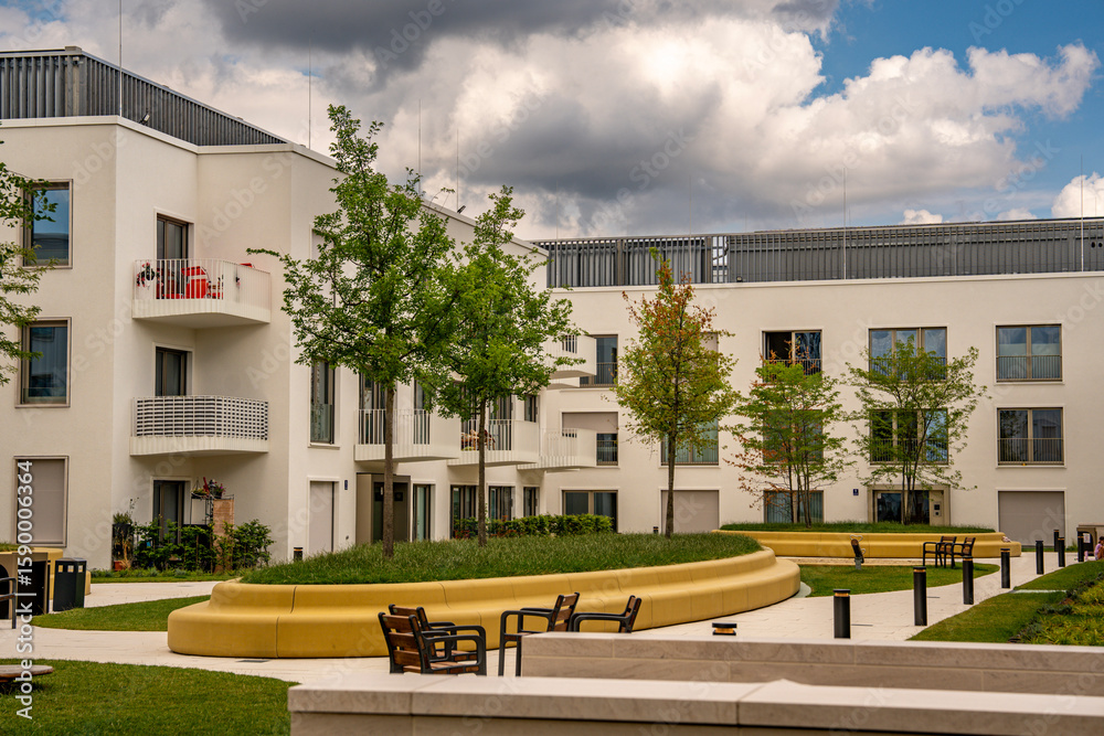 Obraz premium Modern Architecture In Freiham Munich Bavaria: Minimalist Building With Geometric Facade, Large Windows, And Small Tree In Courtyard Under Cloudy Sky