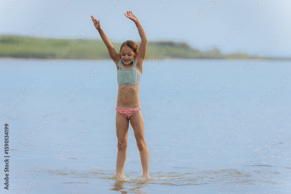 Naklejka premium A young girl jumps high above the water in a powerful split pose, splashing below on a bright summer day, capturing motion, freedom, and joy.
