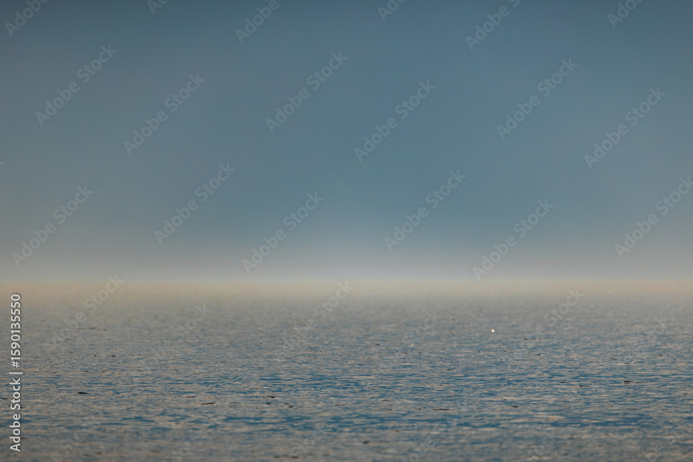 Fototapeta premium Endless ocean horizon sparkles under golden sunlight, blending into a deep blue sky. Calm waters shimmer gently, evoking a sense of peace and infinity.