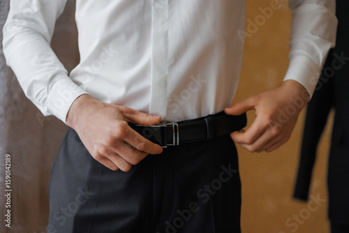 Photography Man adjusting his belt while preparing for a formal event indoors