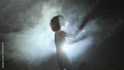 Modern dance, a young woman dancing on a dark background, atmospheric lighting in smoke. A girl in black pants and a mesh blouse performs modern movements in heels