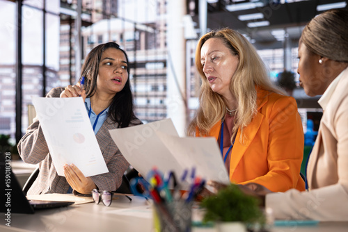 Diverse team of empowered women executives discussing corporate strategy and business growth. Examining analytics to obtain funds for projects, showcasing leadership skills and gender equality.