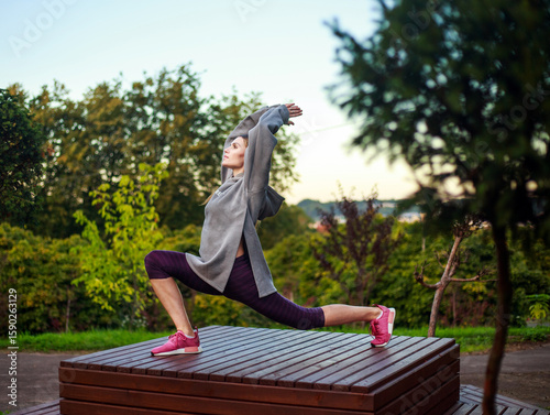 Young attractive woman doing meditation exercises, practicing yoga asana, on background of park and sunset with view of the city