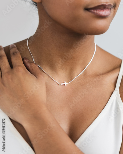 Close up shot of model wearing sideways dainty cross necklace on white background