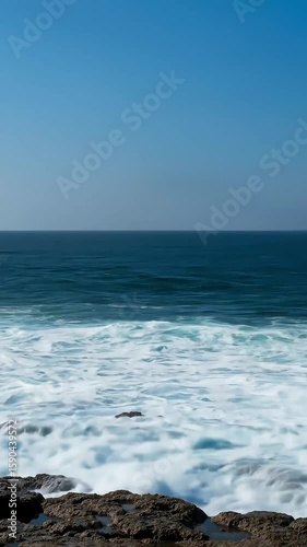 Waves Crashing Against Rocky Coastline Under Bright Blue Sky