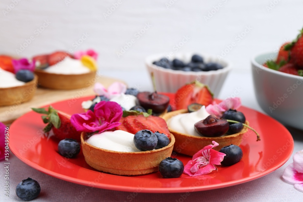 Sweet tartlets with berries and flowers on grey table against light background, closeup. Delicious dessert Sweet tartlets with berries and flowers on grey table against light background, closeup. Delicious dessert
