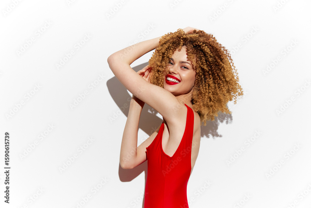 Obraz premium Vibrant portrait of a joyful model in a red swimsuit, showcasing curly hair and a bright smile against a clean white background, symbolizing confidence and summer vibes
