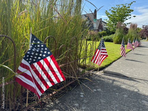 Fototapeta Naklejka Na Ścianę i Meble -  Row of small American flags flutter beside the street, honoring national holidays like Independence Day, Presidents Day, or Veterans Day