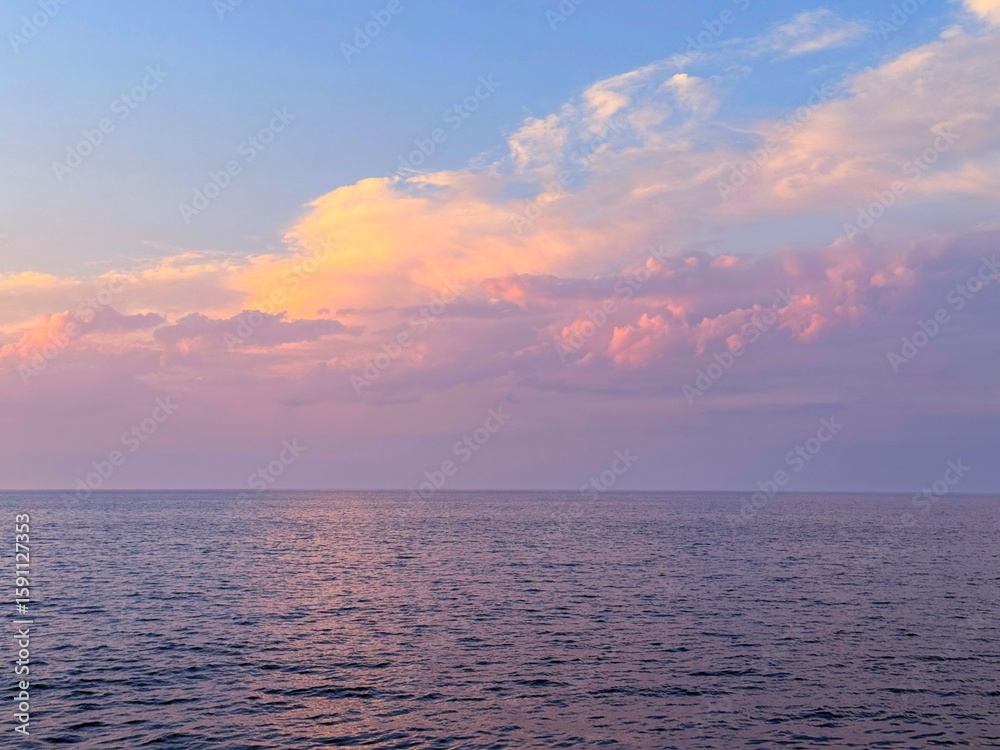 Fototapeta premium Sunrise sky clouds over calm rippling sea water.
