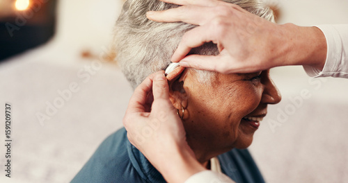 Photos Hands, senior woman and hearing aid with nurse, smile or help with fitting in retirement home