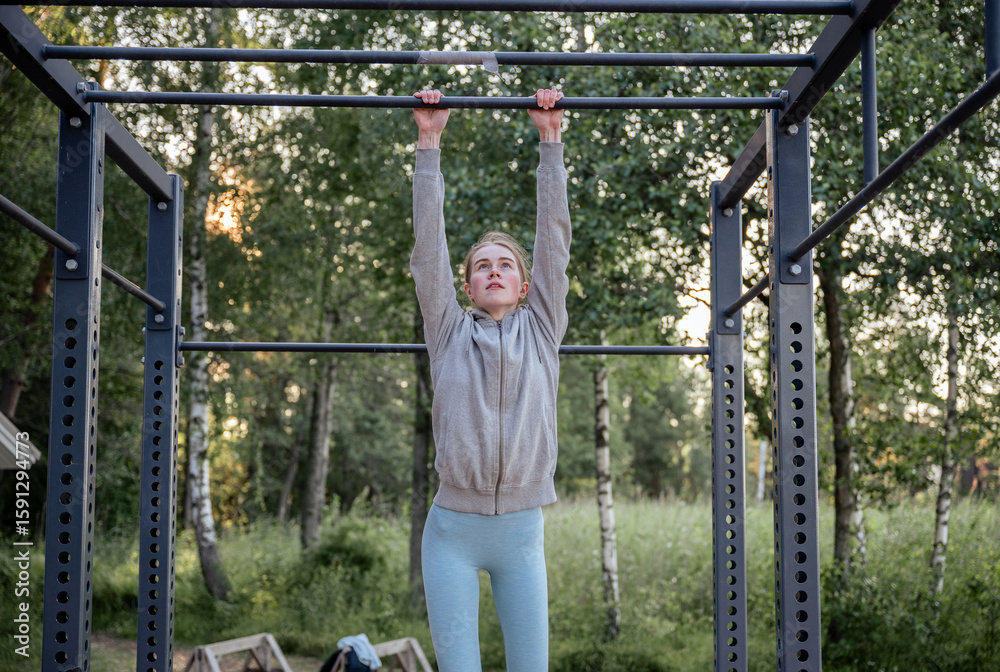 Obraz premium Young woman hanging on pull-up bar at outdoor gym in park