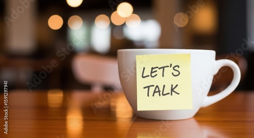 White coffee cup with yellow sticky note saying lets talk on a wooden table