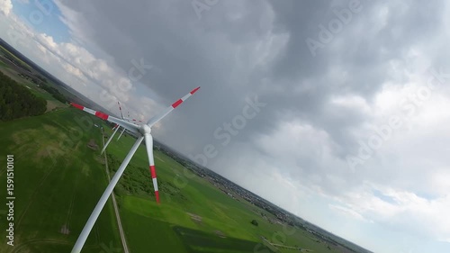 FPV drone flight near spinning wind turbine in a green field. Close-up aerial shot highlighting clean energy production and engineering.