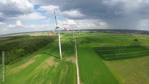 FPV drone flight near spinning wind turbine in a green field. Close-up aerial shot highlighting clean energy production and engineering.