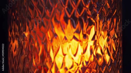 Blurred orange-yellow spots of fire are visible through the patterned frosted glass. A bright candle flame behind a ribbed lampshade..