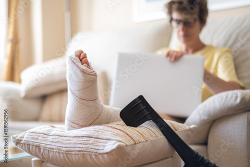 Photos Woman with a broken leg, resting on a cushion with crutches nearby, uses her lap