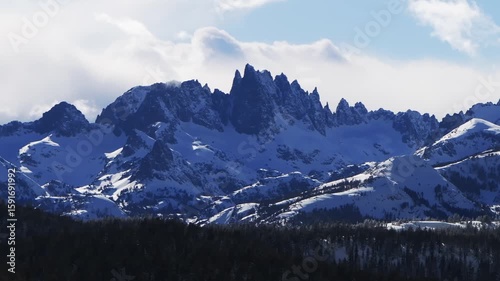 The Hemlocks Mammoth Mountain ski snowboard resort winter sunny blue sky afternoon aerial drone California The Minarets jagged towering peaks fresh deep snow clouds Inyo National Forest static shot