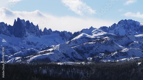 The Hemlocks Mammoth Mountain ski snowboard resort winter sunny blue sky afternoon aerial drone California The Minarets jagged towering peaks fresh deep snow clouds Inyo National Forest pan left