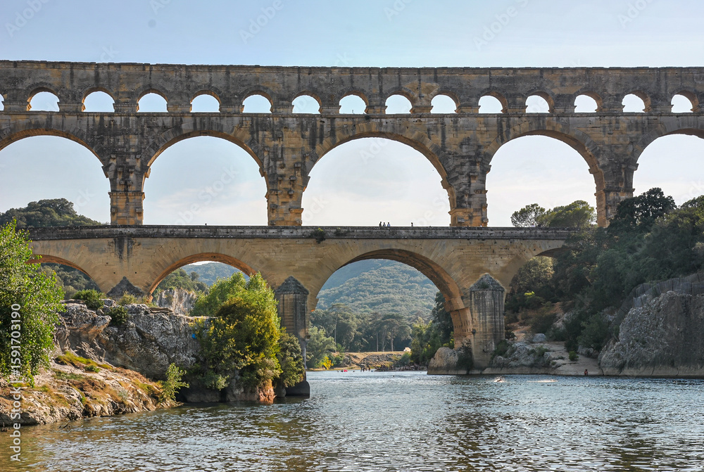 Front view of the Roman aqueduct Pont du Gard above the Gardon River in southern France, seen from water level Front view of the Roman aqueduct Pont du Gard above the Gardon River in southern France, seen from water level